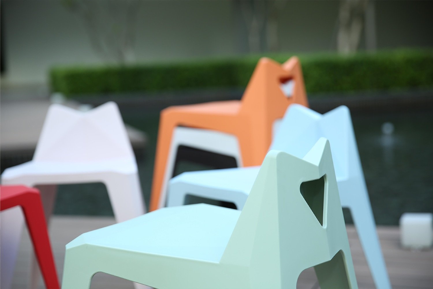 A row of Century chairs in red, white, orange, mint and blue beside a pool