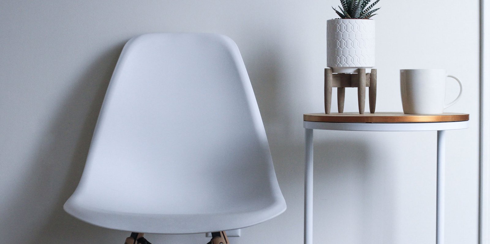 A bright living corner with a Century chair, a potted plant and a mug on a wooden side table